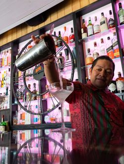 Bartender pouring a cocktail from a shaker into a martini glass at Jazba with a colorful liquor display behind the bar