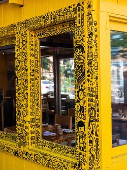 Jazba in East Village shows a yellow wall with black doodles framing a window to the indoor dining space.