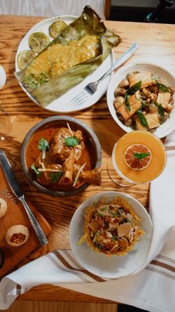 Indian dishes including curry, grilled fish in banana leaf, and cocktails served on a wooden table at Jazba restaurant.