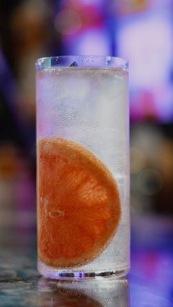 Tall glass cocktail with a slice of grapefruit and sparkling water, set against a colorful blurred background