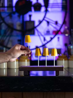 Four yellow cocktail garnishes on sticks arranged on a wooden holder at Jazba bar with clock and bottles in background.
