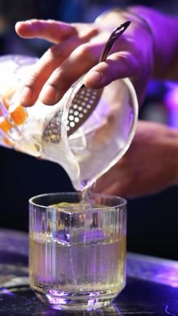 Bartender pouring a cocktail into a glass with ice at Jazba, an Indian cuisine restaurant and cocktail bar.