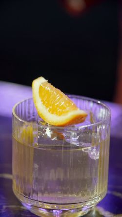 Clear cocktail in a glass with ice cubes, garnished with an orange slice on top, served at Jazba cocktail bar.