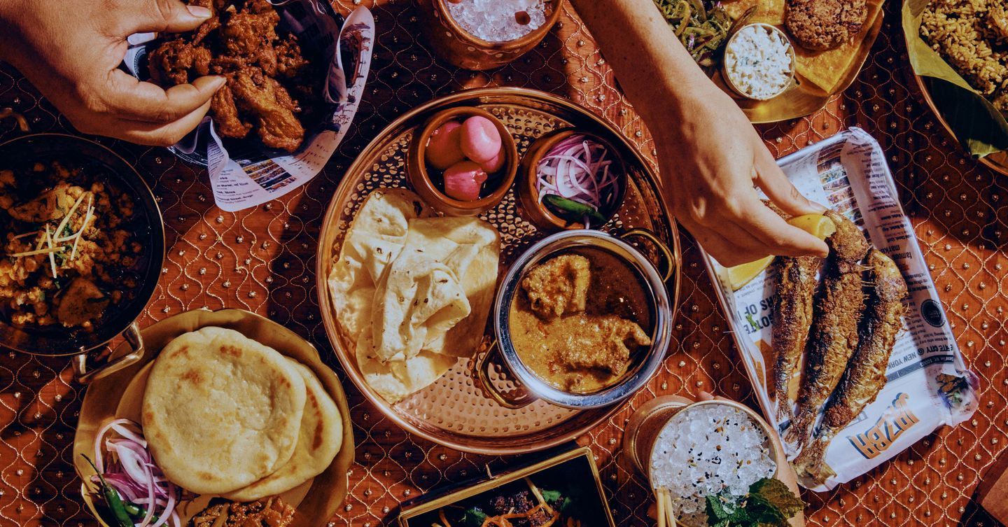 Traditional Indian food spread with naan, curry, fried fish, and pickled onions on a textured tablecloth