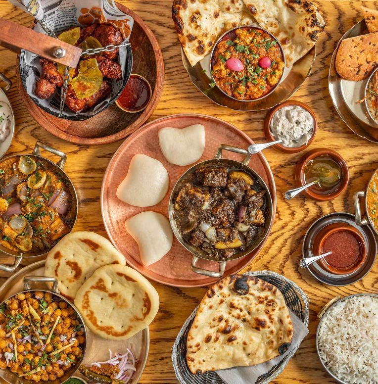 A spread of traditional Indian cuisine including naan, rice, curry dishes, and chutneys on a wooden table at Jazba.