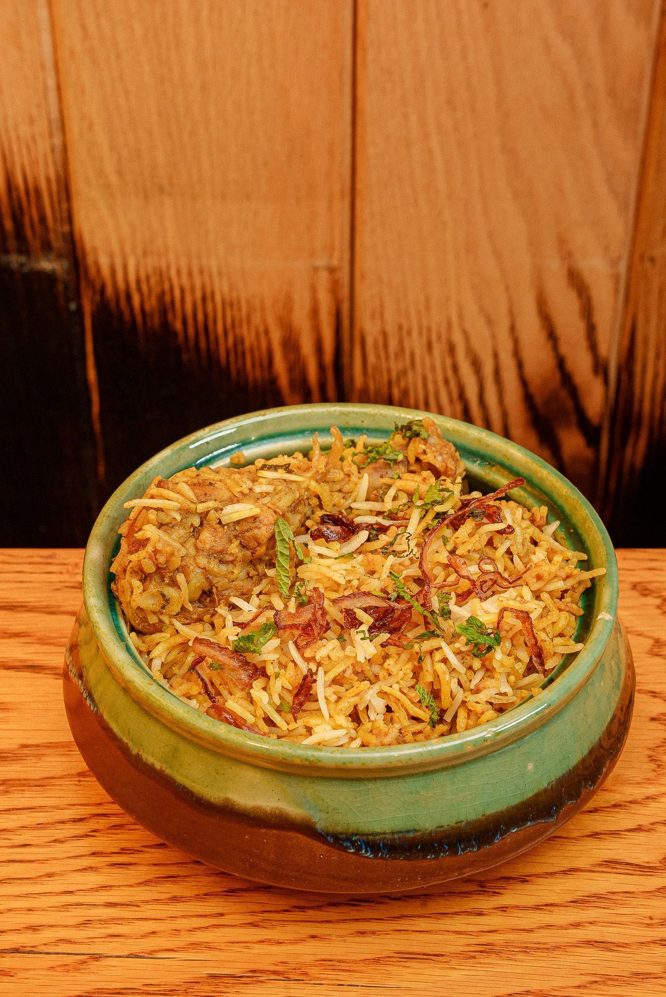 Traditional Indian biryani served in a green ceramic bowl, garnished with fried onions and herbs at Jazba restaurant.